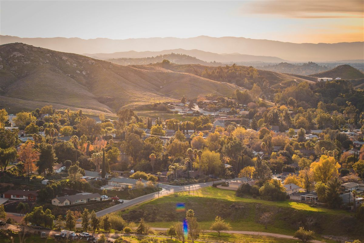 Aerial view of Moreno Valley, California neighborhoods at golden sunset with rolling hills and mountains in the background
